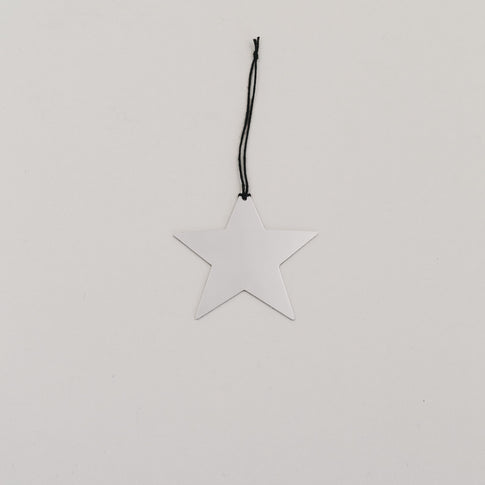 Silberner Sternanhänger aus Metall mit schwarzer Kordel auf hellem Hintergrund, minimalistisch arrangiert.