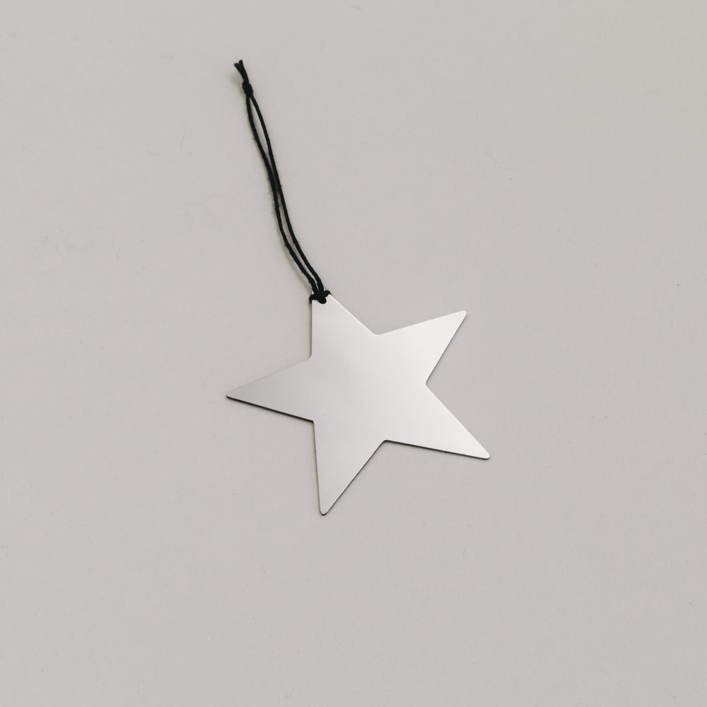 Schlichter silberner Sternanhänger aus Metall mit schwarzem Band, auf hellem Untergrund liegend.