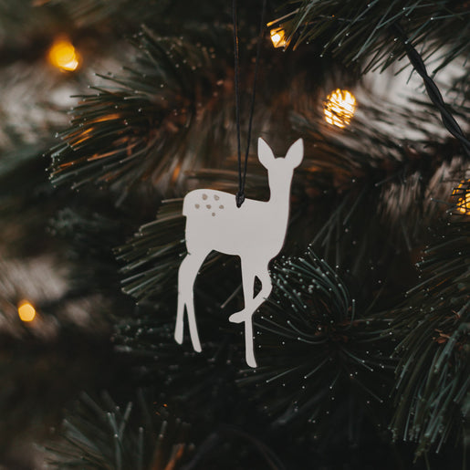 Silberner Rehanhänger  mit schwarzem Band an grünem Tannenzweig, umgeben von warmem Lichterglanz.