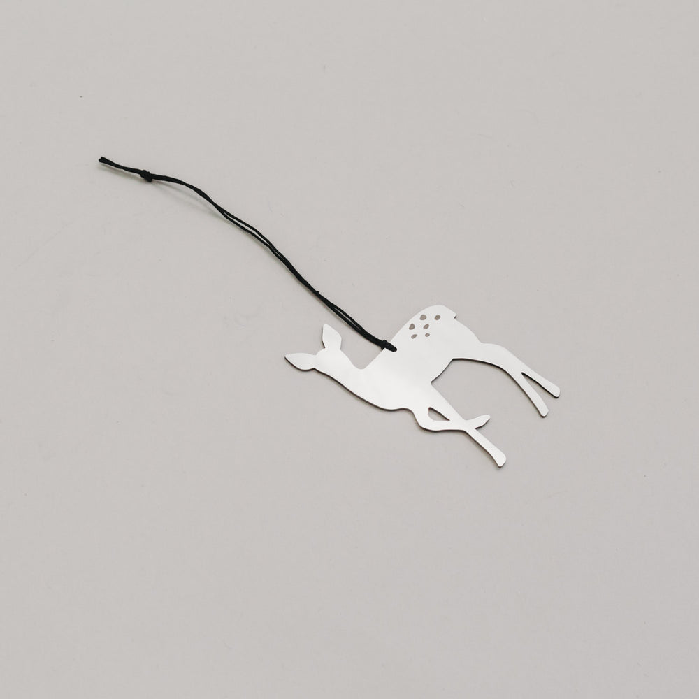 Schlichter silberner Rehanhänger aus Metall mit schwarzem Band, auf hellem Untergrund liegend. 