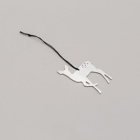 Schlichter silberner Rehanhänger aus Metall mit schwarzem Band, auf hellem Untergrund liegend. 