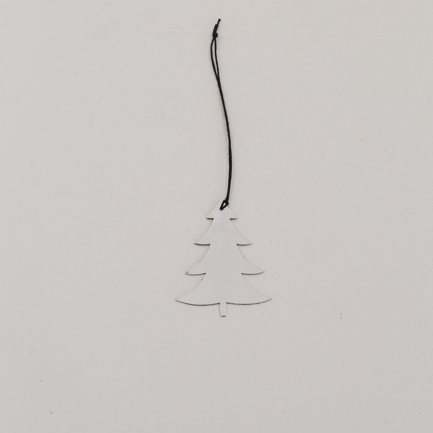 Silberner Tannenanhänger aus Metall mit schwarzer Kordel auf hellem Hintergrund, minimalistisch arrangiert.