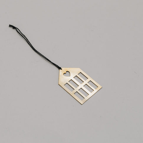 Schlichter goldener Hausanhänger aus Metall mit schwarzem Band, auf hellem Untergrund liegend.