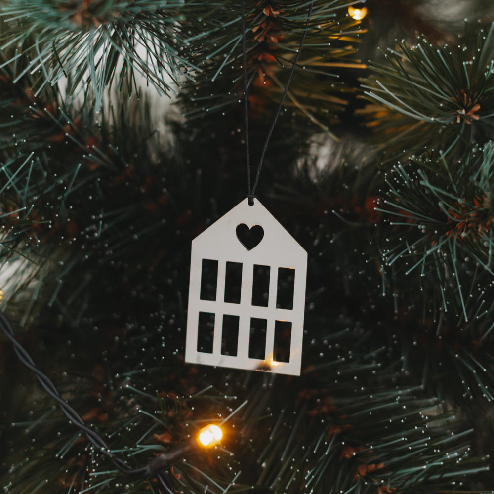 Silberner Hausanhänger  mit schwarzem Band an grünem Tannenzweig.