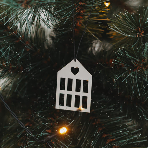 Silberner Hausanhänger  mit schwarzem Band an grünem Tannenzweig.