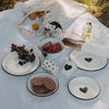 Weißer Emaille-Becher mit schwarzem Herzmuster im sommerlichen Picknick-Setting mit passendem Emaille-Geschirr.