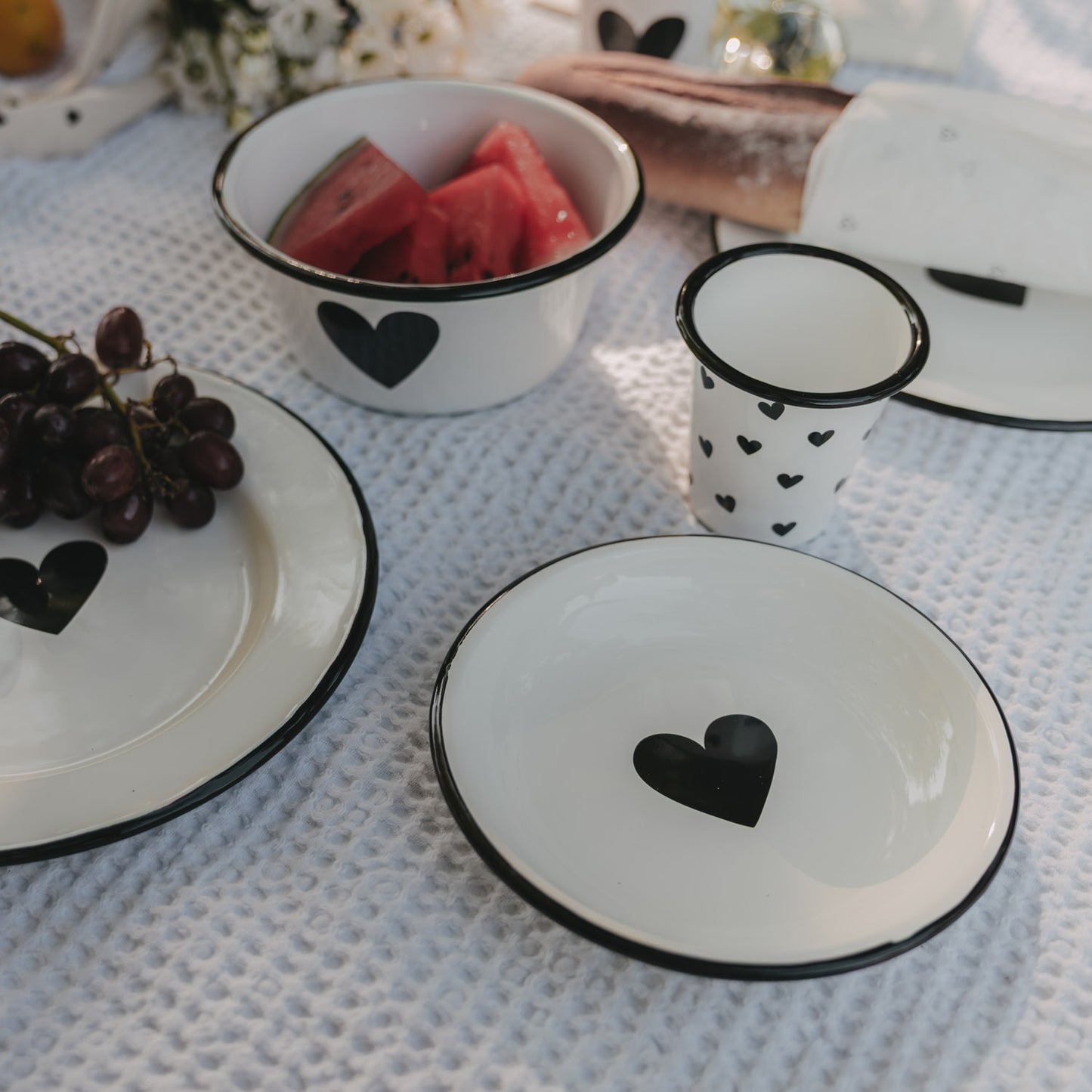 Weißer Emaille-Frühstücksteller mit schwarzem Herz im sommerlichen Picknick-Setting mit passendem Emaille-Geschirr.