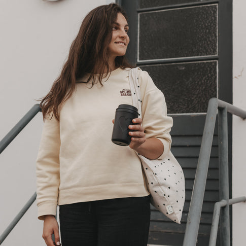 Frau mit schwarzem To-Go-Becher mit Herzmotiv von Eulenschnitt und Stofftasche auf einer Treppe