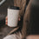Cremefarbener To-Go-Becher mit Herzmotiv und schwarzem Deckel in der Hand einer Frau