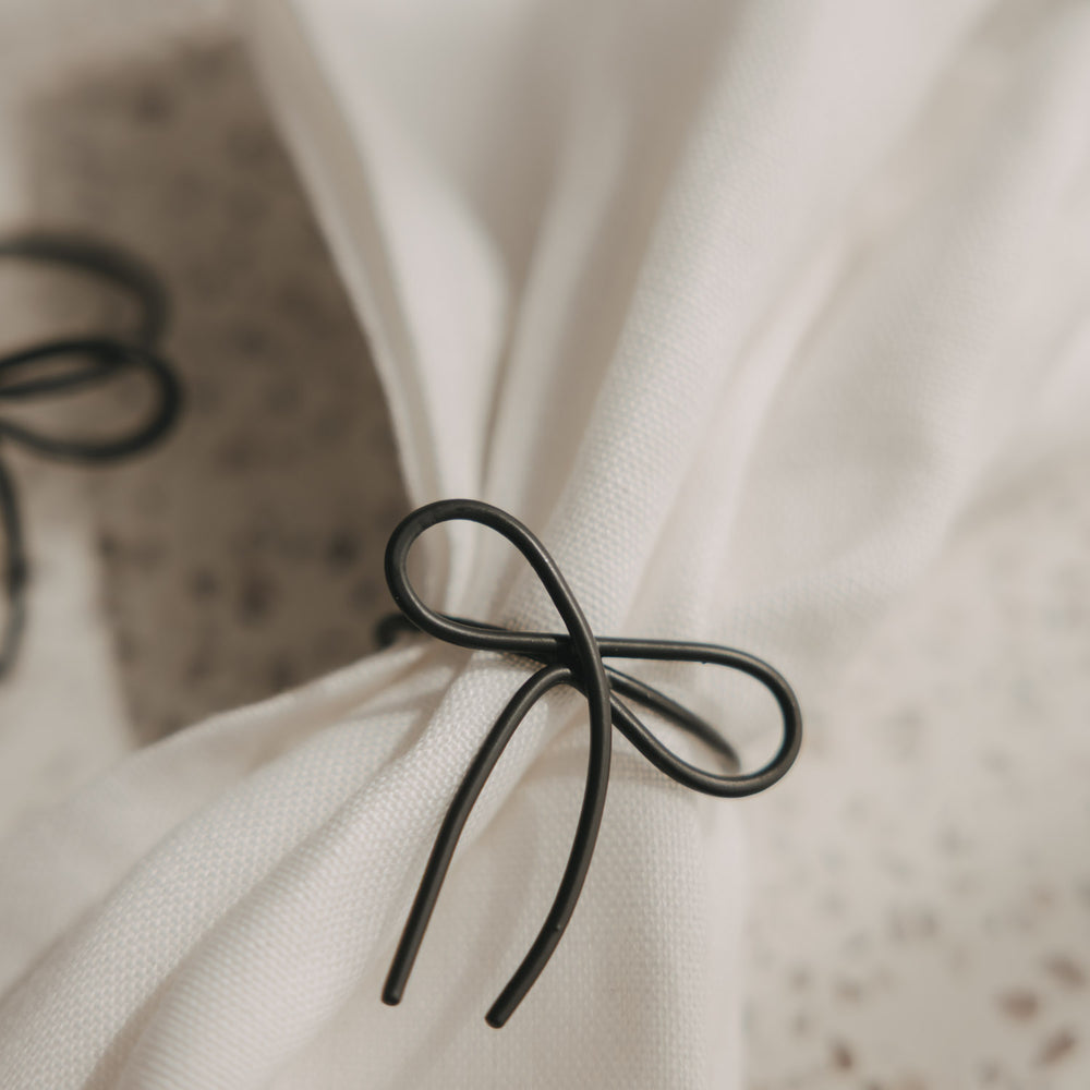 Detailaufnahme des Serviettenrings Schleife in Anthrazit an einer weißen Stoffserviette.
