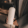 Trinkflasche Herz in Creme mit 500 ml Fassungsvermögen , schwarzem Deckel und geprägtem Herzmotiv in der Hand einer Frau