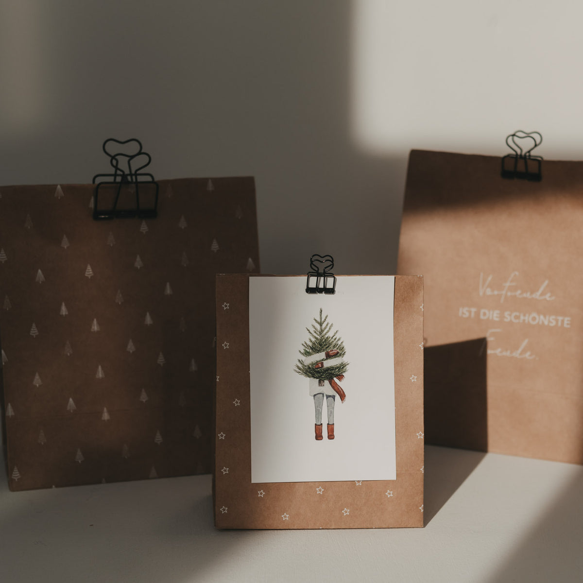 Schwarze Herz-Clips an drei braunen Geschenktüten mit Weihnachtsmotiven und einer Grußkarte.