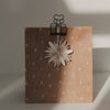 Schwarzer Herz-Clip hält eine braune Geschenktüte mit Tannenbaummuster und weißem Papierstern zusammen.