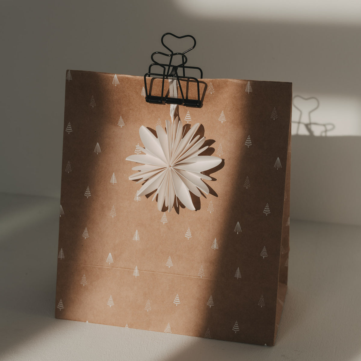 Schwarze Foldback-Klammer mit Herzgriffen an einer braunen Weihnachtstüte mit weißen Tannenbäumen und Papierstern.