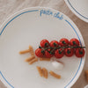 Speiseteller „pasta club“ mit hellblauem Rand, dekoriert mit Cherrytomaten, Fusilli und Knoblauch auf hellem Leinentisch.