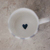 Blick in eine Tasse mit schlichtem weißem Inneren und kleinem dunkelblauen Herz am Boden.