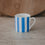 Kleine Tasse mit hellblauen, vertikalen Streifen und zartem Henkel vor neutralem Hintergrund mit Holzbrett.