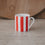 Kleine Porzellan-Tasse mit roten Streifen frontal auf heller Fläche, weicher Hintergrund mit Holzbrett.