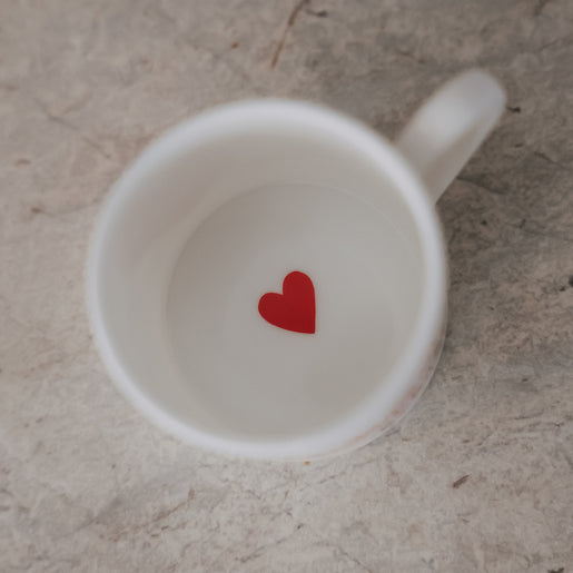 Draufsicht in die kleine weiße Tasse – am Boden ein kleines rotes Herz auf heller Steinoberfläche.