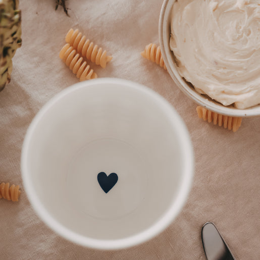 Weißer Herz-Becher von oben, neben Pasta und cremigem Gericht, stilvolle Keramik Tasse mit Herzmotiv