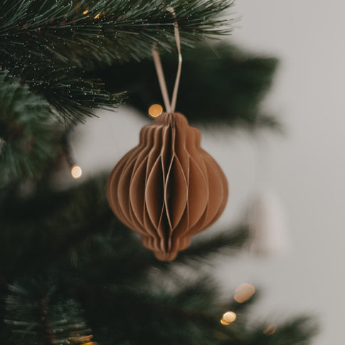 Papieranhänger in Braun hängt an einem festlich geschmückten Weihnachtsbaum mit zartem Lichterglanz.