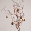 Natürliche Papieranhänger in Ei- und Hasenform hängen an dekorativen Zweigen in einer Vase.
