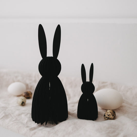 Schwarze Papierhasen im 2er-Set als Deko, arrangiert mit Eiern und Frühlingselementen auf Stoff.