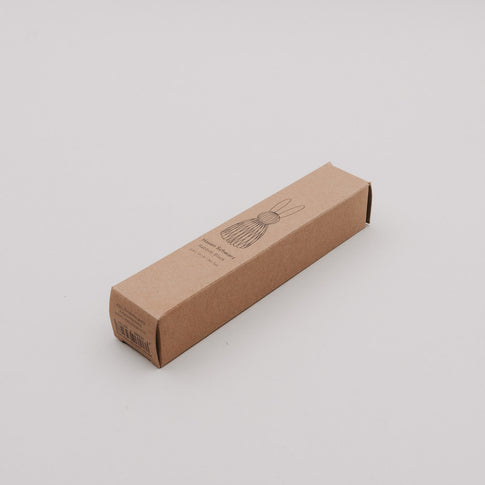 Schmale Kartonverpackung für schwarzen Papierhasen, schlichtes Design mit gezeichneter Hasenillustration.