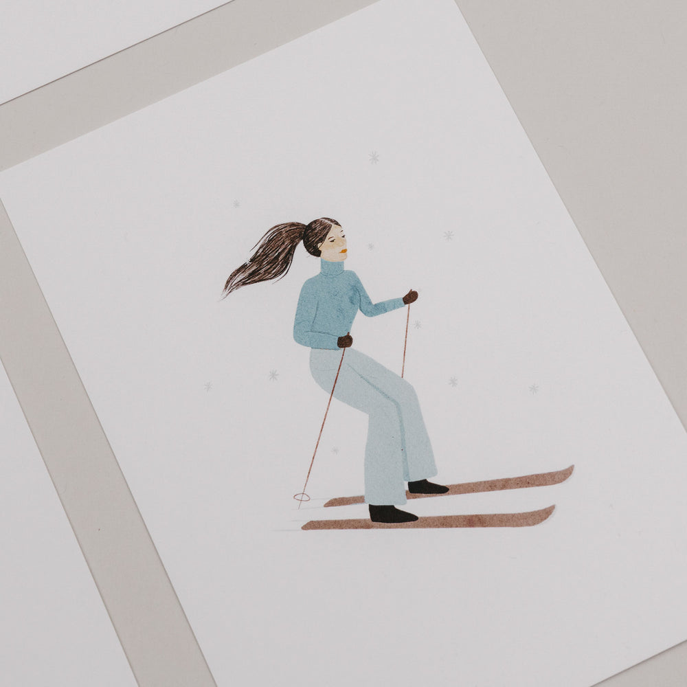 Weihnachtskarte mit einer Frau auf Skiern in blauer Winterkleidung vor weißem Hintergrund