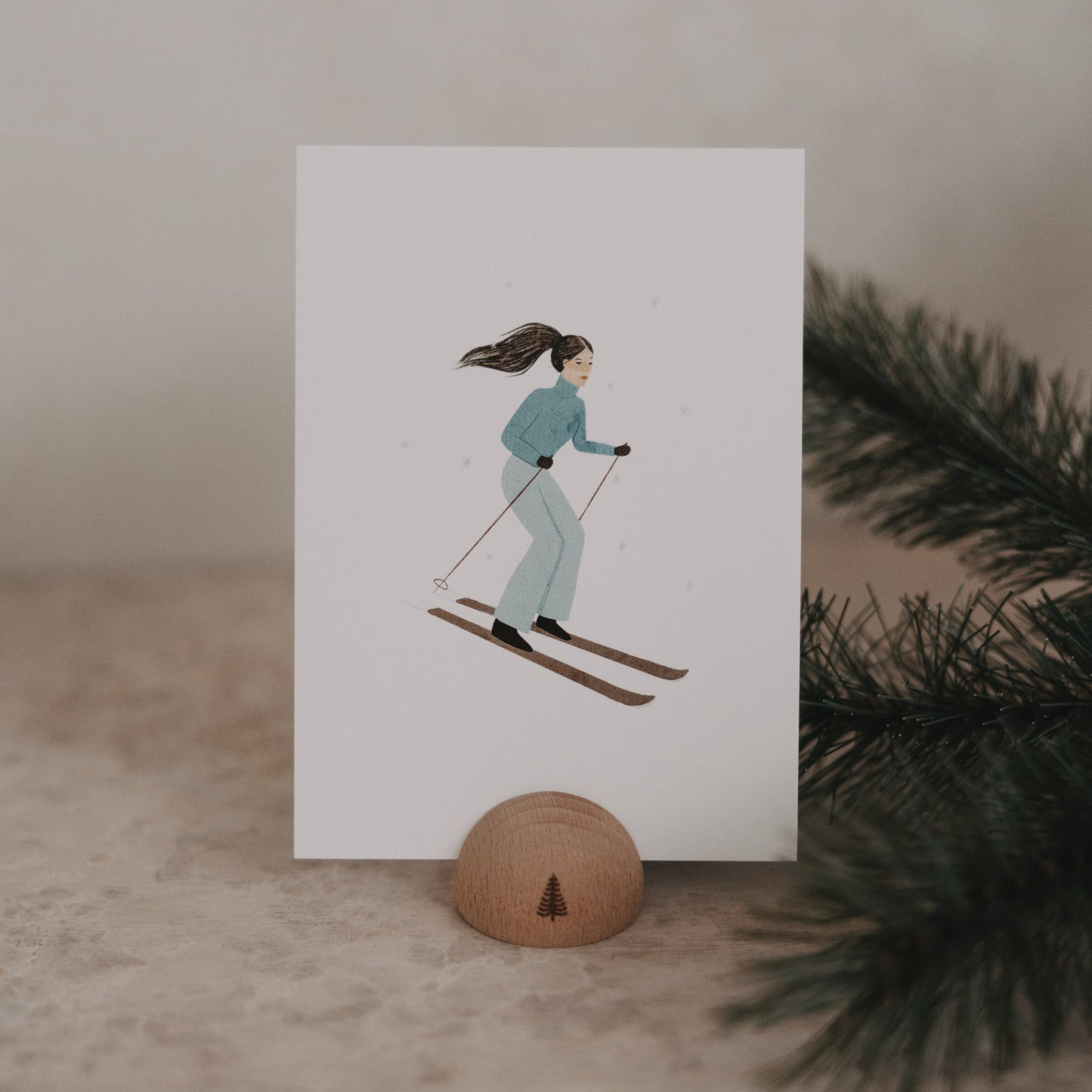 Weihnachtskarte mit einer Frau auf Skiern in blauer Winterkleidung vor weißem Hintergrund