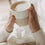Beiger Keramikbecher „Hello New Day“ mit Herz und Milchschaum, in beiden Händen gehalten