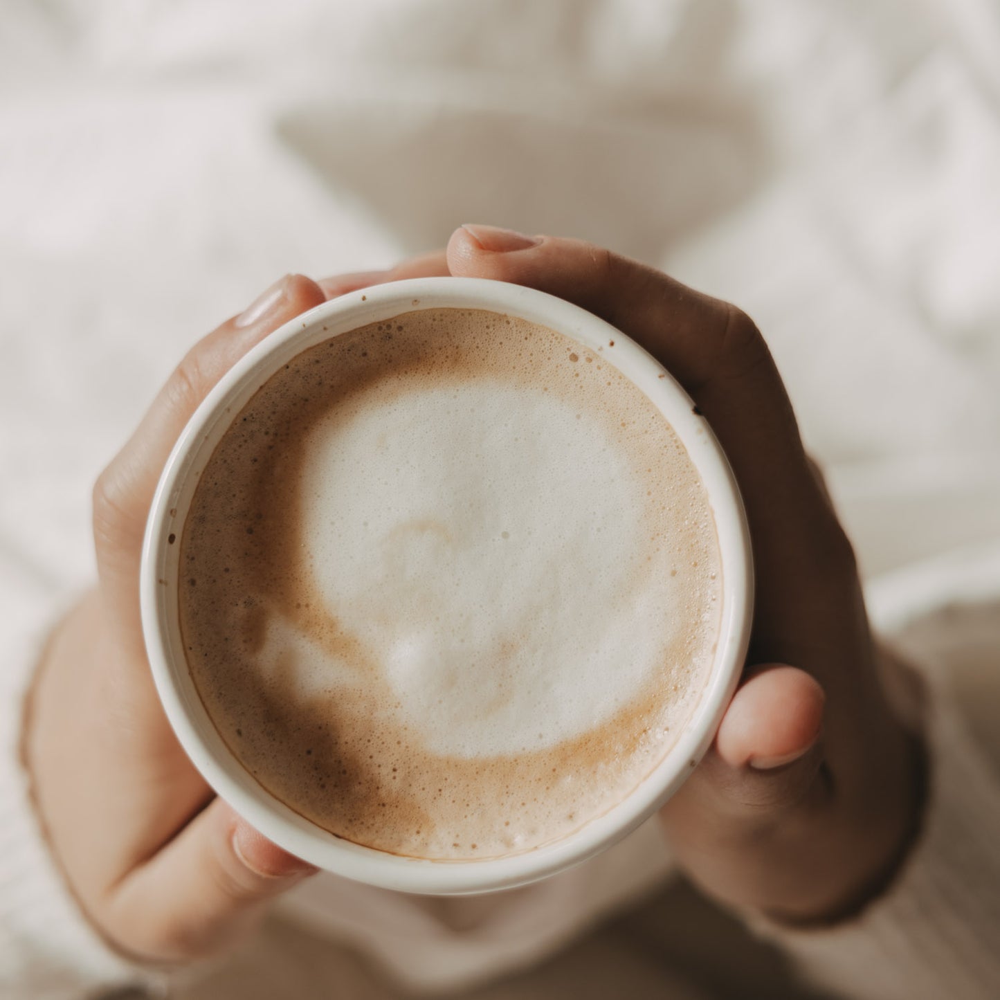 Keramikbecher „Hello New Day“ mit aufgeschäumtem Kaffee, von oben in beiden Händen gehalte