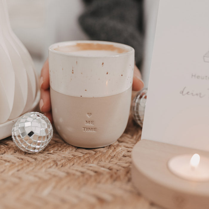 Keramikbecher „Me Time“ mit Herz, Cappuccino und kleiner Discokugel neben einem brennenden Teelicht