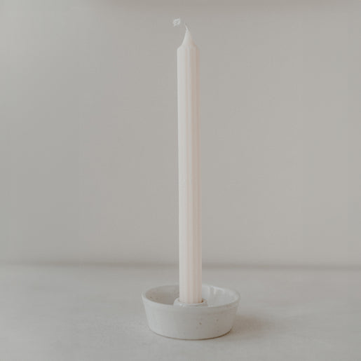 inzelner cremefarbener Stabkerzenhalter mit schlichter, matter Glasur in Natursteinoptik, in dem eine helle Stabkerze steht. Fotografiert vor neutralem, weichem Hintergrund mit ruhiger Lichtstimmung.
