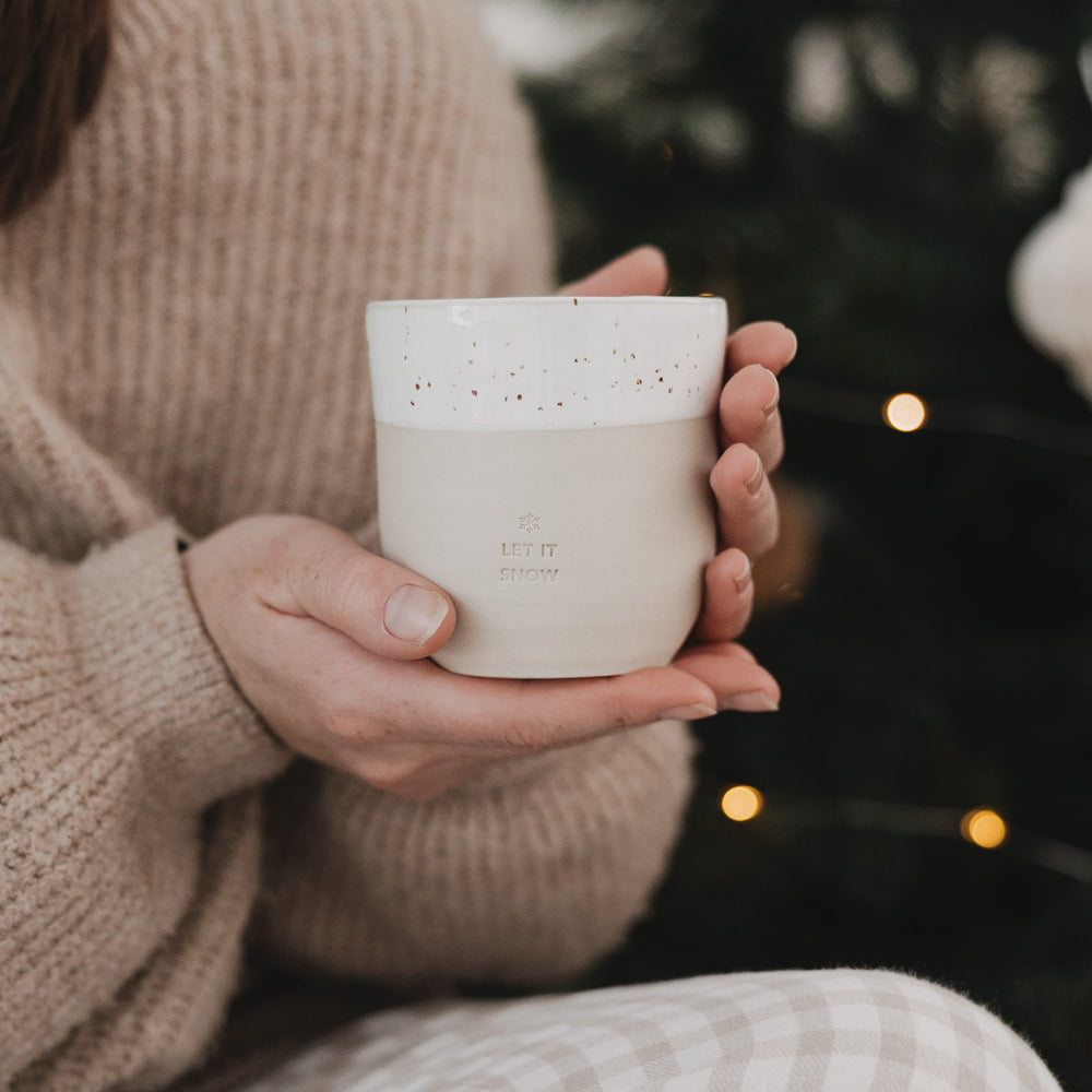 Person hält Becher „Let it Snow“ aus Steingut mit Sprenkeln, gemütliche Winterstimmung.
