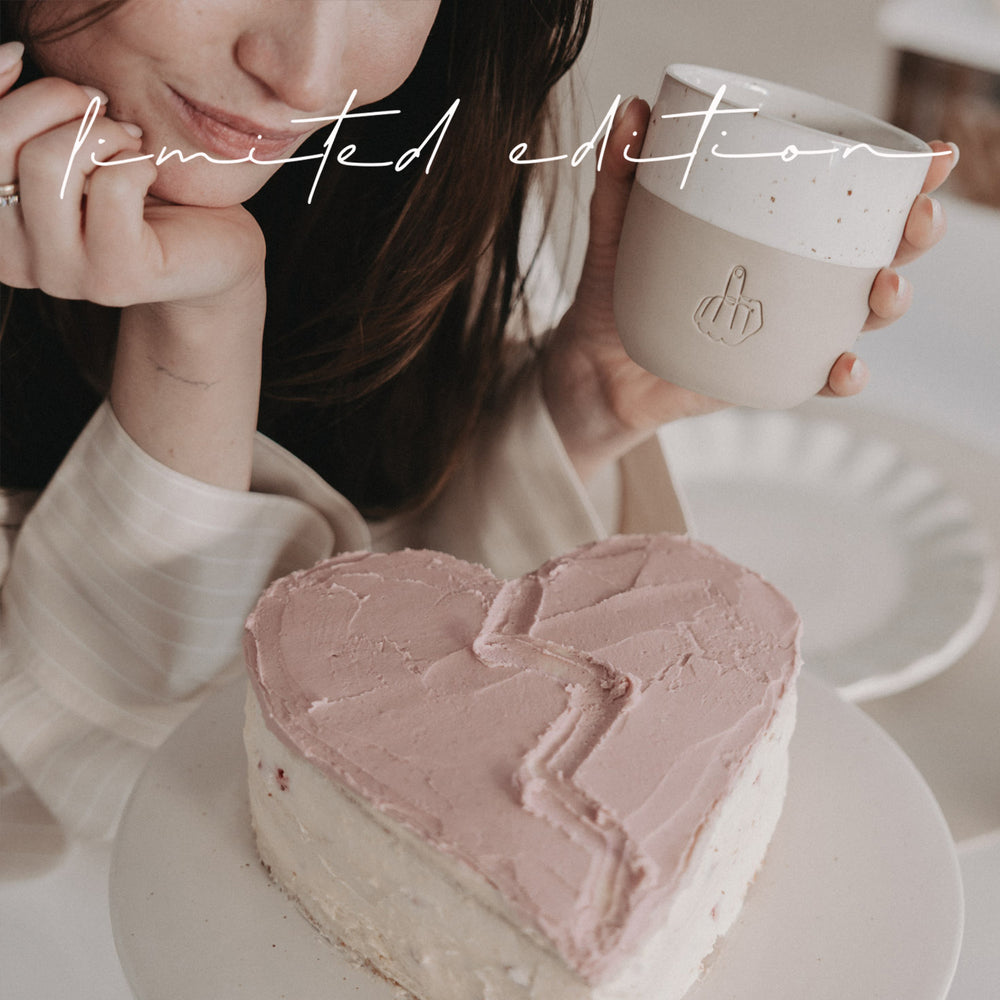 Limitierter Becher „Nein Danke“ mit Mittelfinger-Motiv, Person hält Becher neben herzförmigem Kuchen, Valentinstag Edition.