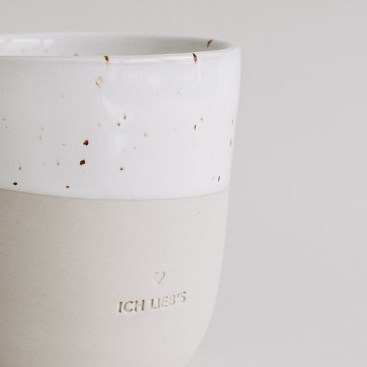 Nahaufnahme der „Ich lieb’s“-Tasse mit heller Glasur und Sprenkeln, Fokus auf Prägung.