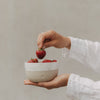 Beige-weiße Keramikschale mit Herz und frischen Erdbeeren, in den Händen gehalten