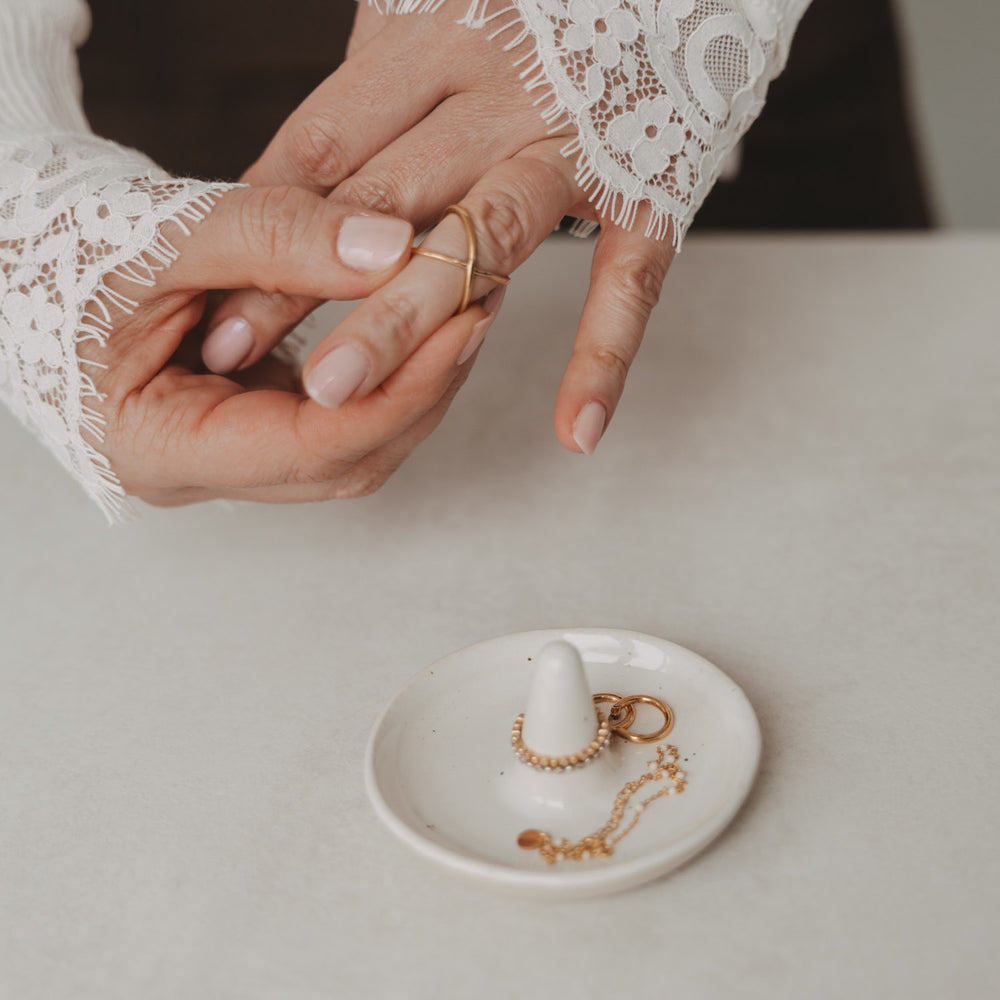 Weiße Keramik-Schmuckablage mit Ringhalter, Kette und Ringen neben Händen mit Goldring