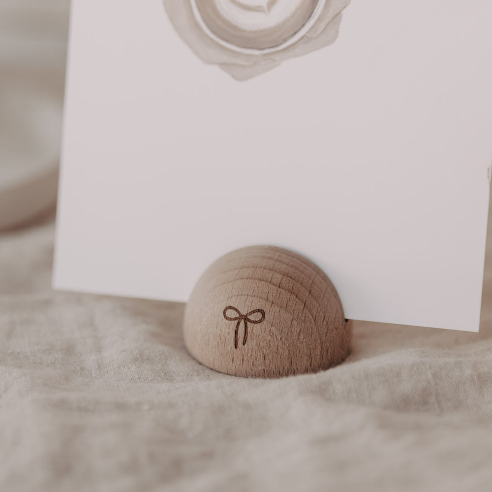 Detailansicht des halbrunden Kartenständers mit Schleifen-Gravur aus Holz auf hellem Leinenstoff