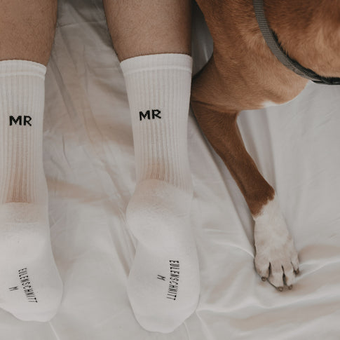 Detail weißer Socken „MR“ am Fuß neben einem Hund auf Stoff