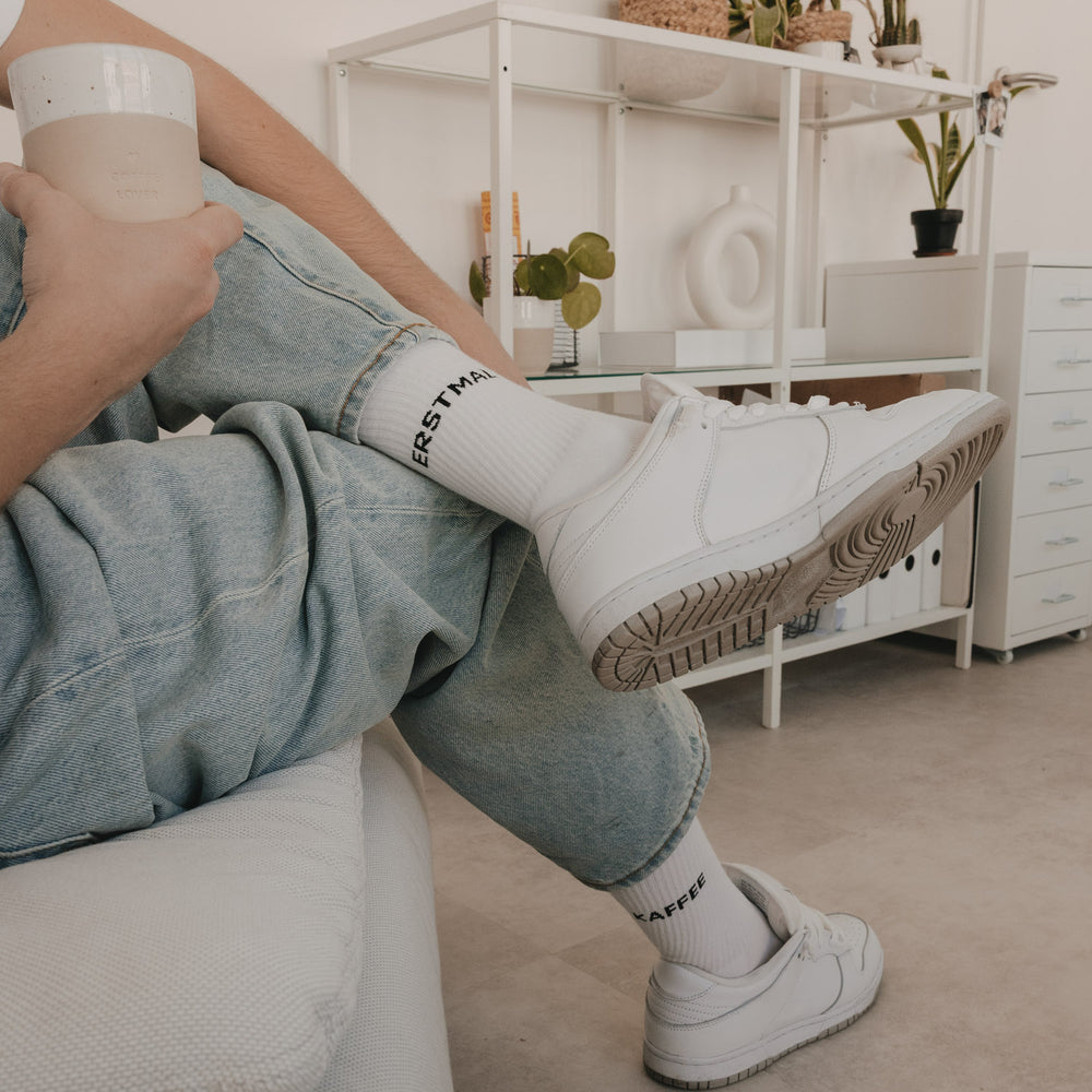 Weiße Socken „Erstmal Kaffee“ kombiniert mit Sneakern im gemütlichen Wohnraum
