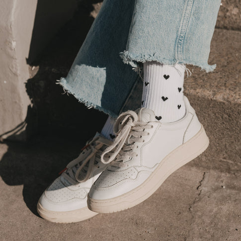 Weiße Socken mit schwarzen Herzchen kombiniert mit Sneakern und Jeans im Sonnenlicht