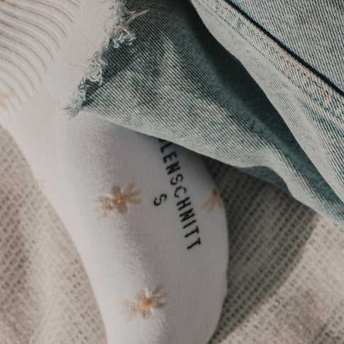 Detailansicht weißer Socken mit Gänseblümchen und Eulenschnitt Schriftzug
