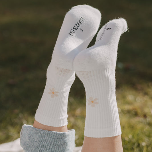 Weiße Socken mit Gänseblümchen-Motiv entspannt getragen im Freien auf Wiese