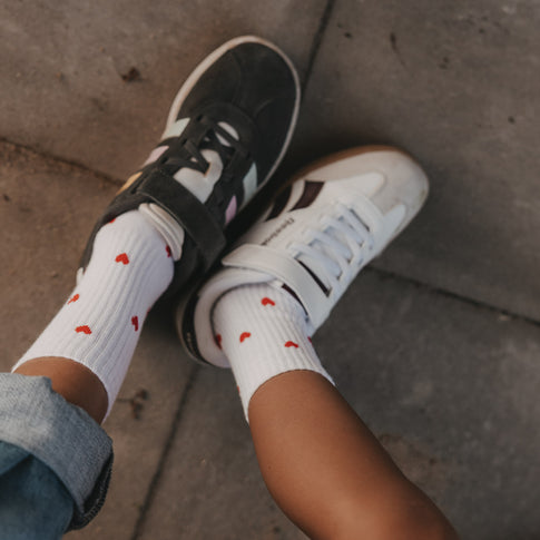 Weiße Eulenschnitt Kindersocken mit roten Herzen im Allover-Design und Sneakern.