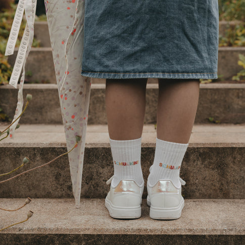 Kind steht auf Treppe mit weißen Socken „Schulkind“ und Sneakern, Schultüte daneben