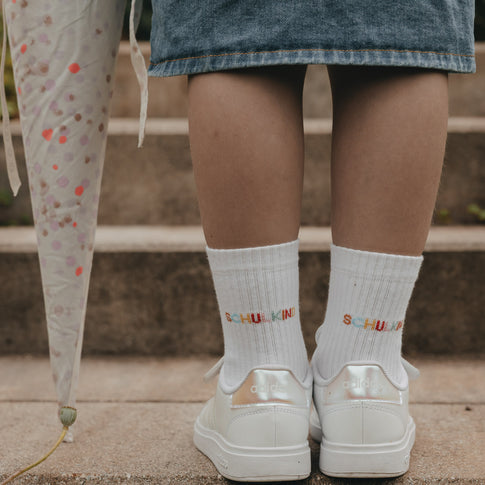 Detail Socken „Schulkind“ auf Treppe, weiße Sneaker und bunter Schriftzug sichtbar
