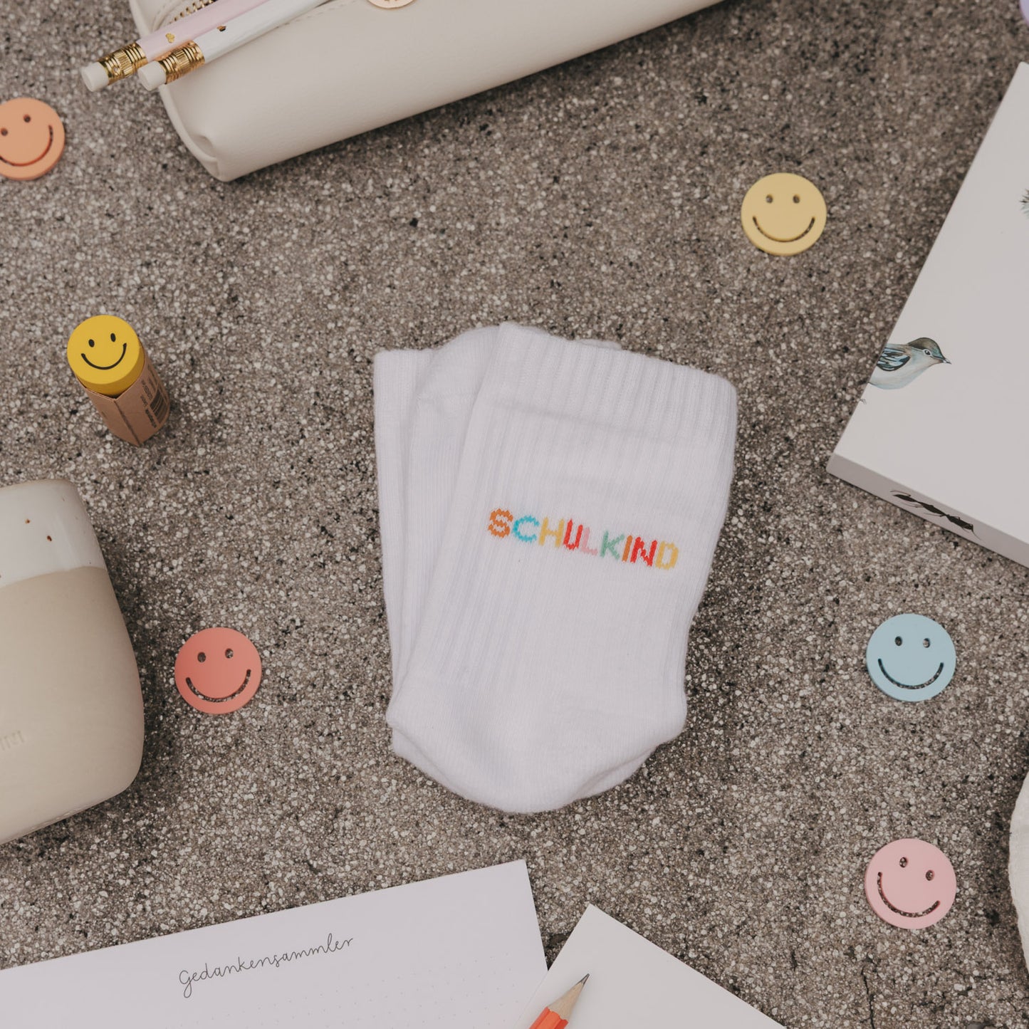 Produktbild weiße Socken „Schulkind“ flach liegend, umgeben von Schulutensilien