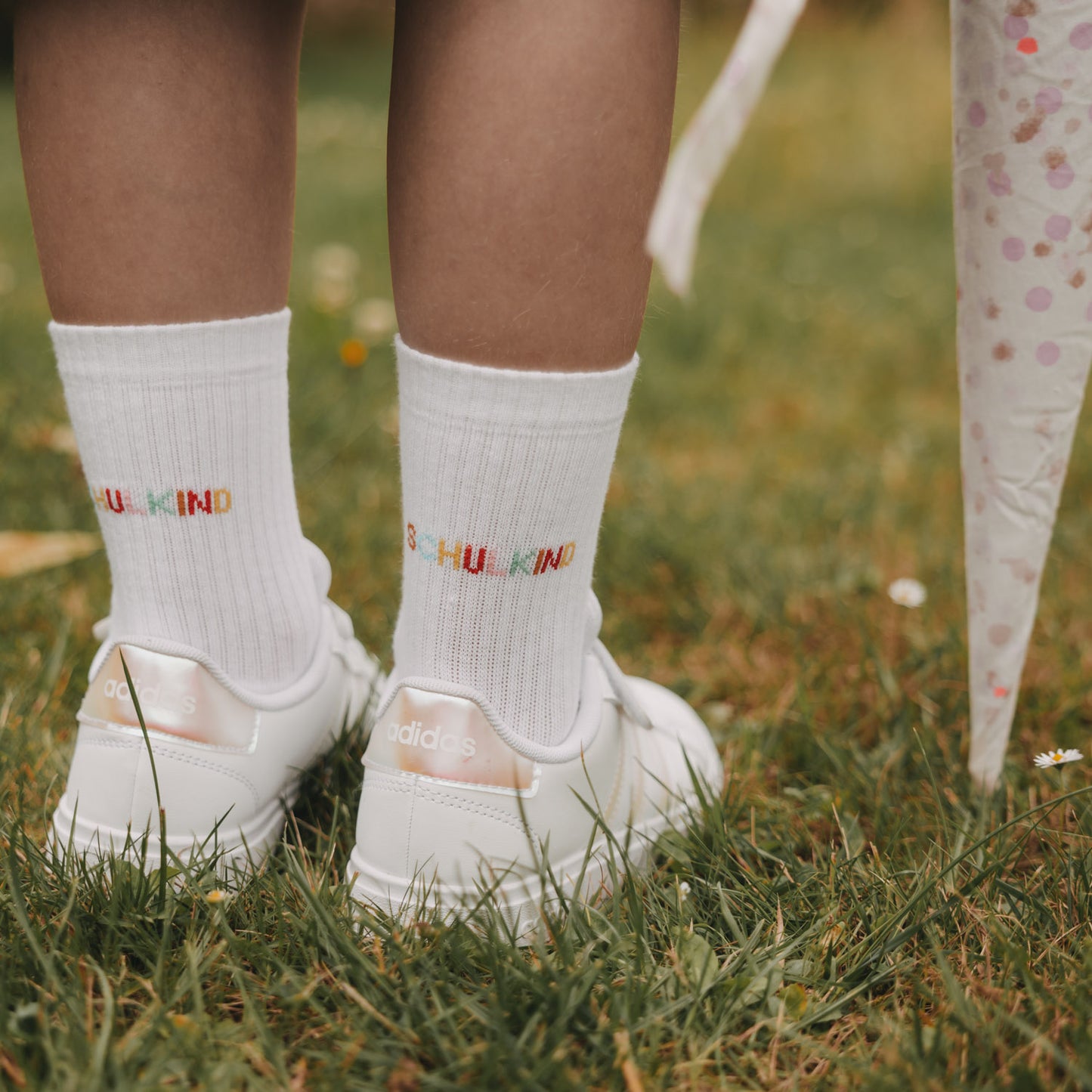 Detailansicht weiße Socken „Schulkind“ mit buntem Schriftzug, getragen auf Wiese
